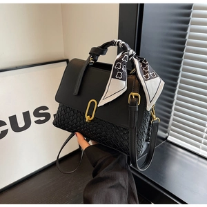 Detailed macro view of black crossbody bag featuring woven texture and silk scarf on handle