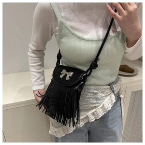 Detail of a black crossbody bag with silver bow accent and long fringe tassels