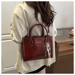 Detail of burgundy textured square handbag featuring elegant gold lettering and chocolate charm