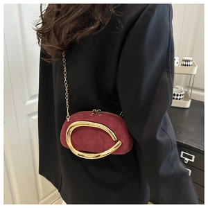 Detail of burgundy suede shoulder bag featuring a prominent gold lip-shaped metal handle