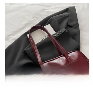 Detail of burgundy leather handbag with dual handles and artistic beaded pendant