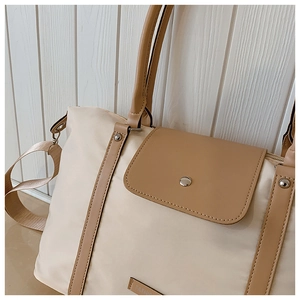Close-up of cream nylon tote bag with brown leather trim and FASHION metal plaque