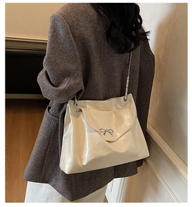 Close-up of beige tote bag featuring silver bow metal buckle and elegant chain strap