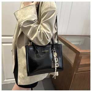 Détail d'un sac cabas en cuir noir brillant avec un pendentif chaîne à rayures chic