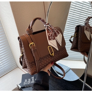 Detail of brown tote bag featuring woven texture, silk scarf handle, and gold metal buckle