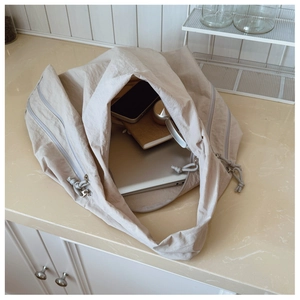 Spacious beige nylon shoulder bag showing interior capacity for a laptop and books