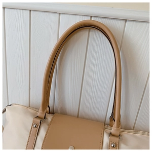 Close-up of cream nylon tote bag with brown leather handle and metal rivet details