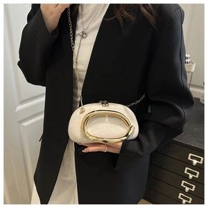 Close-up of cream crossbody bag featuring a large gold buckle and metal chain strap