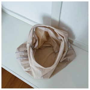 Detail of spacious beige nylon crossbody bag featuring side zipper compartments and soft texture
