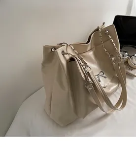 Detail of beige tote bag featuring metal chain strap and decorative bow buckle closure