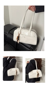 Detail of white glossy leather shoulder bag with beaded charm and front buckled pocket
