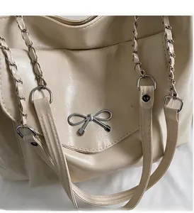 Detail of cream tote bag showing silver metal bow charm and textured leather surface