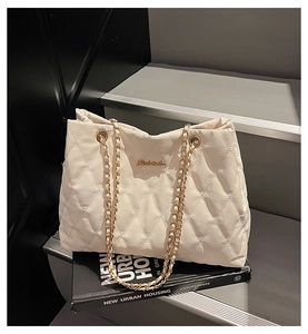 Close-up of quilted beige tote bag with gold chain straps and sleek metallic logo