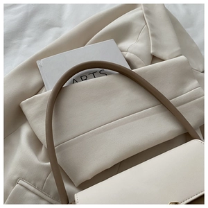 Gros plan du sac en cuir crème avec poignées marron sur un blazer beige élégant