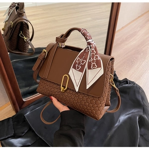 Close-up of brown woven leather handbag with decorative silk scarf on handle