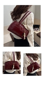 Detail view of burgundy faux leather shoulder bag with decorative bead keychain on a model