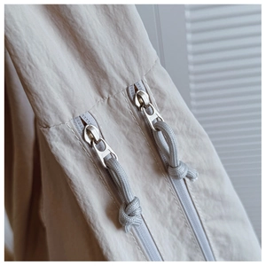 Detail view of double zippers with grey knotted pulls on a beige crossbody bag