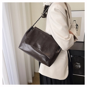Détail de la texture cuir froissé marron foncé et bandoulière chaîne d'un grand sac porté épaule