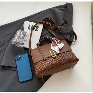 Detail of brown woven leather bag with gold buckle, printed scarf, and adjustable strap