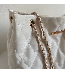 Detail of quilted beige shoulder bag with gold chain strap and metallic logo hardware
