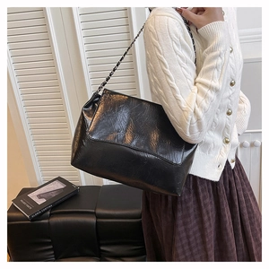 Vue latérale d'un sac à chaîne plissé noir brillant sur un modèle avec fond blanc épuré