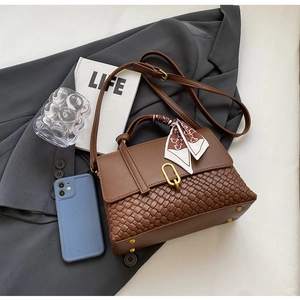 Detail of a brown leather bag featuring woven textures, silk scarf and gold buckle