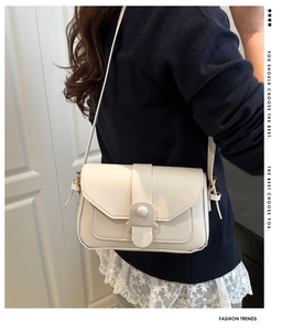 Close-up of cream crossbody square bag with unique buckle and strap on a model