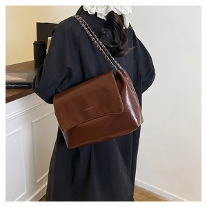 Détail du sac à bandoulière en cuir verni marron foncé avec texture froissée vintage