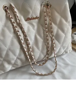 Detail of white quilted handbag with a golden chain strap and smooth faux leather finish