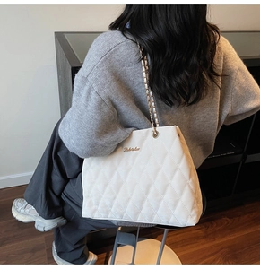 Detail of white quilted tote bag featuring a gold metal logo and classic diamond pattern