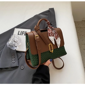 Detail of green textured handbag with brown leather flap and silk scarf accent