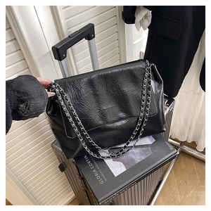 Détail du sac à bandoulière noir à texture froissée avec chaîne argentée sur une valise