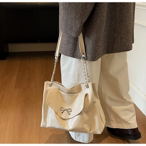Detail of cream tote bag featuring a metallic bow buckle and leather chain shoulder strap