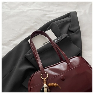 Detailed close-up of dark burgundy tote bag with wooden bead charm on a white sheet
