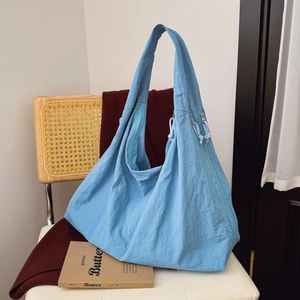 Blue nylon hobo bag with large capacity and drawstring detail on a cozy wicker chair