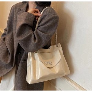 Close-up of cream shoulder bag featuring a metallic bow clasp and chain strap