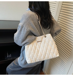 Close-up of white quilted tote bag with golden metal logo and woven chain strap