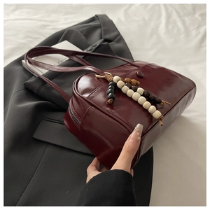 Close-up of deep red leather tote bag with unique wooden bead charm and metal zipper