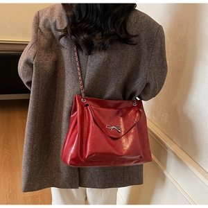 Detail of red PU leather tote with silver metal bow and chain strap on shoulder