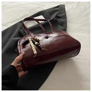 Detailed shot of dark red glossy shoulder bag featuring beaded charm and vintage strap