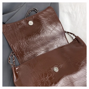 Détail du sac à chaîne marron foncé avec texture en cuir froissé brillant et fermoir magnétique