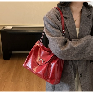 Close-up of red glossy leather shoulder bag with a silver bow metal buckle detail