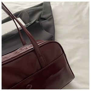 Close-up of wine red faux leather Boston bag with smooth mirror finish and zipper detail