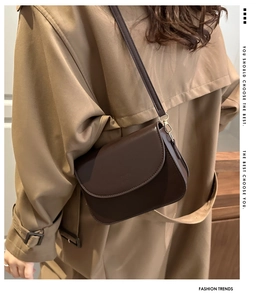 Close-up of dark brown leather crossbody bag with gold hardware worn on shoulder