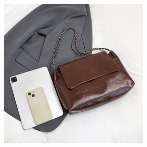 Détail du sac bandoulière en cuir ciré marron foncé avec chaîne argentée et texte gaufré