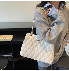 Detailed close-up of white quilted tote bag featuring gold chain strap and metal logo