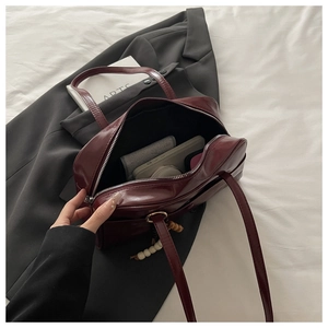 Detail of burgundy glossy tote bag with wood bead charm on black blazer and white sheet