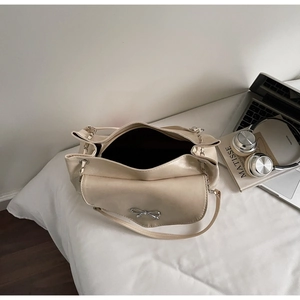 Detail of cream leather shoulder bag featuring a silver bow ornament and chain strap