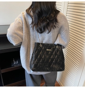 Detail of black quilted shoulder bag with gold chain strap and elegant metal logo