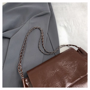 Détail du sac bandoulière en cuir plissé marron avec chaîne argentée et logo embossé